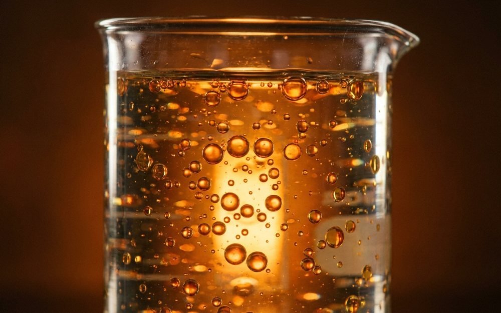 Golden droplets suspended in a clear liquid, backlit in a laboratory beaker